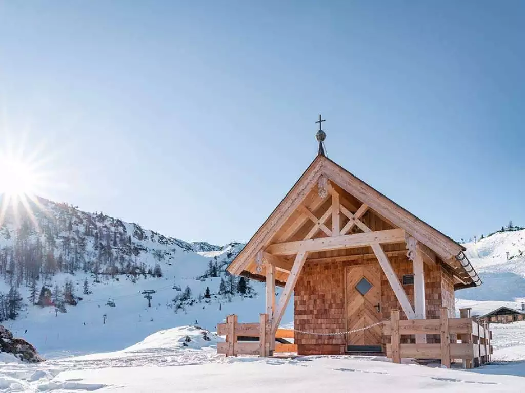 Holzkapelle in Winterlandschaft mit Bergpanorama