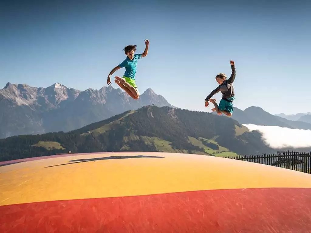 2 Kinder springen auf einem Luftkissen mit Berge im Hintergrund