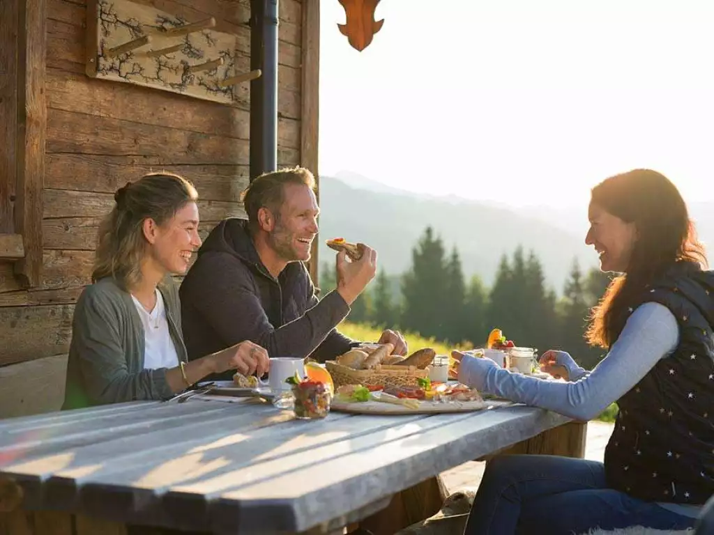 2 Frauen und 1 Mann genießen Jause auf einer Berghütte