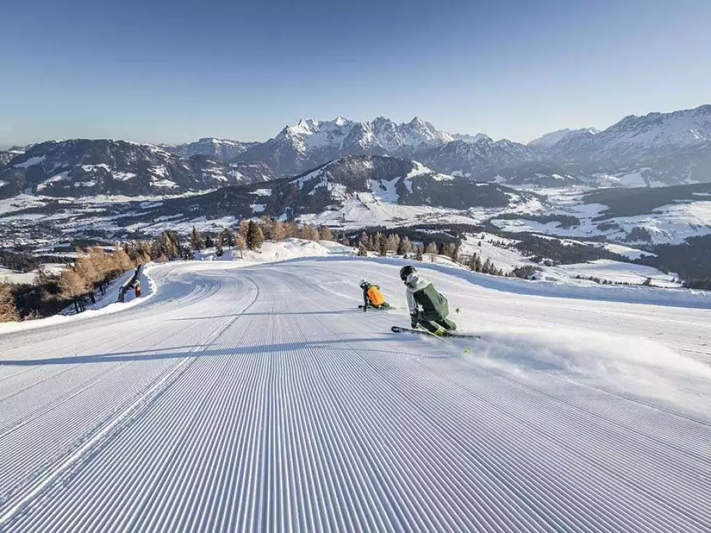 2 Skifahrer bei Abfahrt auf Piste mit Bergpanorama